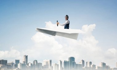 Korkmuş pilot, ağzı açık, kağıt düzlemde oturuyor ve direksiyonu tutuyor. Havacı mavi gökyüzünde iş merkezi üzerinde kağıt uçak sürüş. Yüksek gökdelenler ve ofis binaları ile Cityscape.