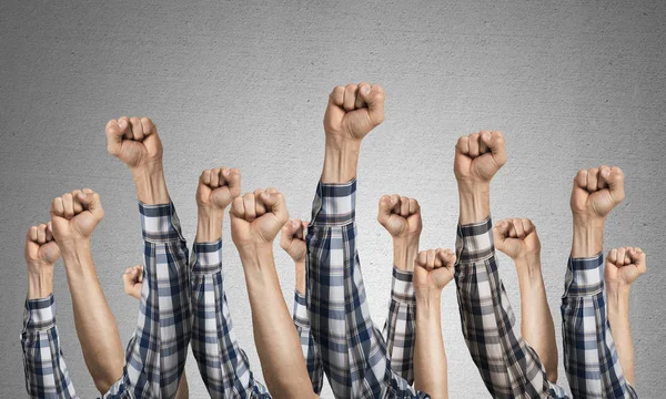 Row of man hands showing clenched fist gesture. Victory or protest group of signs. Human hands gesturing on background of grey wall. Many arms raised together and present popular gesture.