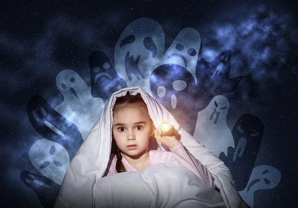 Scared girl with flashlight hiding under blanket from imaginary ghosts. Kid sitting in bed on night sky background. Covered child in pajamas not sleep at night. Mysterious phantoms in darkness.