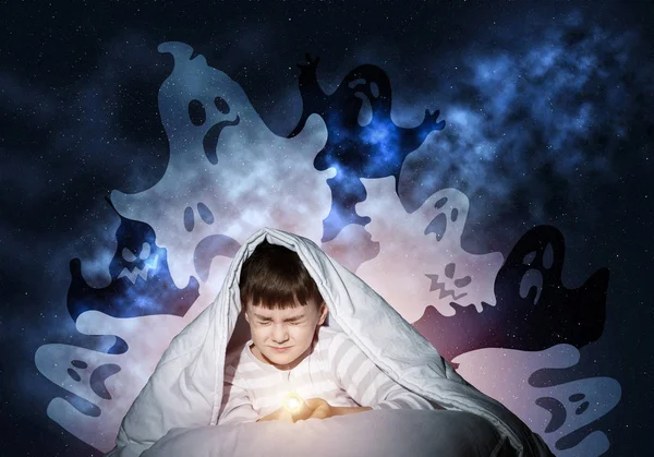 Scared boy hiding under blanket from imaginary spooky monsters. Fearful kid with closed eyes lying in his bed at home. Little boy afraid of nightmares. Covered child in pajamas not sleep at night.