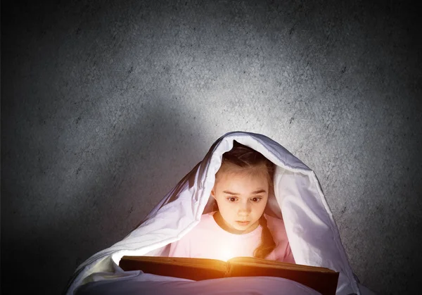 全神贯注的小女孩睡觉前在床上看书 漂亮的孩子 手电筒藏在毯子下 灰色墙壁背景上穿着睡衣的漂亮女孩 儿童阅读童话 — 图库照片
