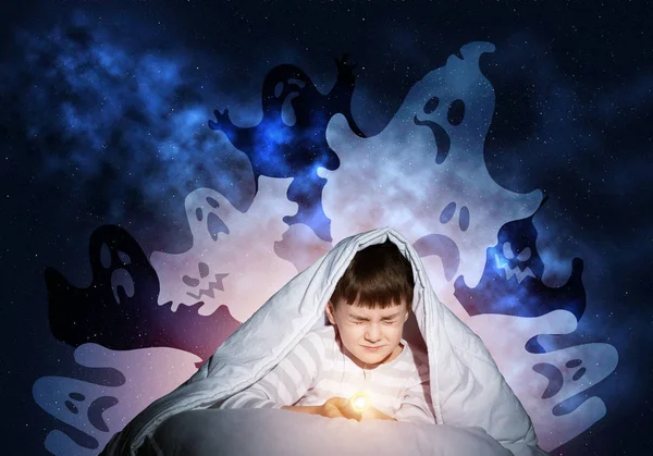 Scared boy hiding under blanket from imaginary spooky monsters. Fearful kid with closed eyes lying in his bed at home. Little boy afraid of nightmares. Covered child in pajamas not sleep at night.