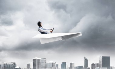 Havacı şapkalı işadamı ve gözlükler fırtınada kağıt uçak sürüyor. Kriz yönetimi kavramı. Küçük kağıt uçak pilot yan görünümü. Dramatik karanlık bulutlu gökyüzü ile Megalopolis panorama.