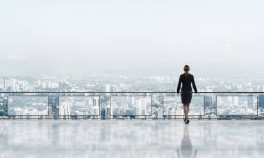 Balkonda takım elbiseli genç bir iş kadını sabah şehir manzarasına karşı.