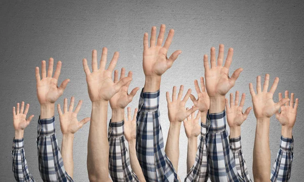 Row of man hands showing five spread fingers gesture. Hello or help group of signs. Human hands gesturing on background of grey wall. Many arms raised together and present popular gesture.