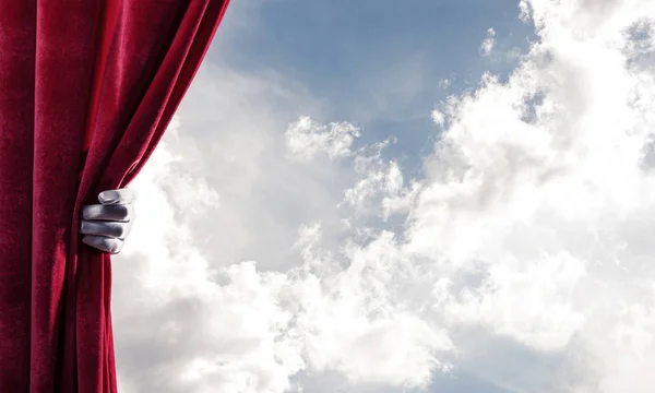 赤いカーテンの後ろの曇った風景とそれを保持する手 — ストック写真