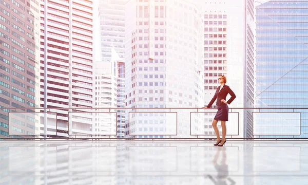 Balkonda takım elbiseli genç bir iş kadını sabah şehir manzarasına karşı.