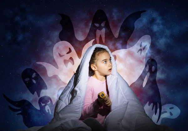 Worried girl hiding under blanket from imaginary ghosts. Scared kid sitting in his bed at home. Little girl afraid of fantasy monsters. Covered child in pajamas not sleep at night. Halloween holiday.