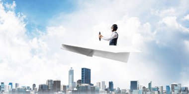 Kağıt uçakta oturan pilot ile iş motivasyonu kavramı. Havacı şapkalı komik adam ve şehrin üzerinde kağıt uçak süren gözlükler. Rüyada gökyüzünde uçmak. Yüksek binalarile modern megapolis.
