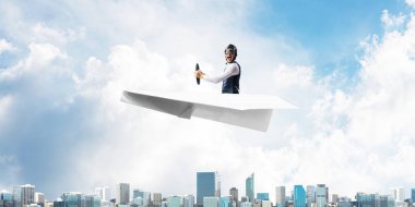 Kağıt uçakta oturan pilot ile iş liderliği ve motivasyon konsepti. Havacı şapkalı komik adam ve şehrin üzerinde kağıt uçak süren gözlükler. Yüksek binalarile modern megapolis.