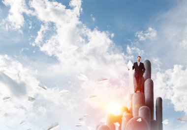 Takım elbiseli hırslı ve genç işadamı, arka planda bulutlu gökyüzü manzarası olan stune sütununda dururken elinde büyük beyaz bir afiş tutuyor.