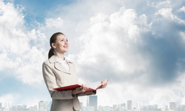 Şehir manzarası ve mavi gökyüzü arka planda açık defter tutan çekici kadın. Elinde açık kitap ile beyaz iş elbisesi zarif genç kadın. Şirkette staj ve uygulama.
