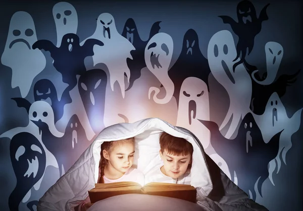 热情的小女孩和男孩睡后在床上看书 穿着睡衣的孩子用手电筒一起躲在毯子下 深蓝色背景上的恐惧儿童和假想的怪物 — 图库照片