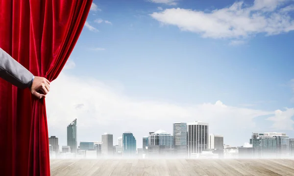 Ciudad de negocios en niebla gris detrás de la cortina roja y la mano sosteniéndolo — Foto de Stock