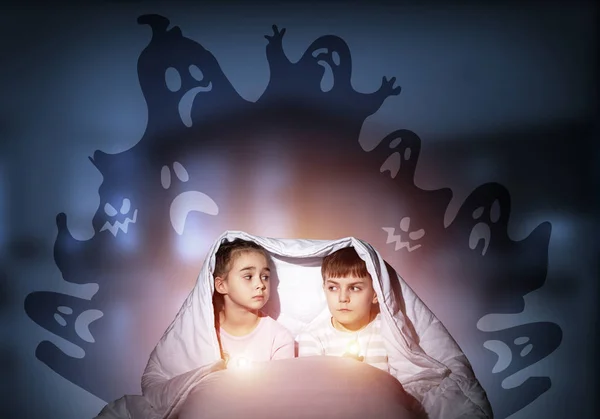 害怕的姐姐和弟弟用手电筒躲在毯子下 躲避恶梦般的怪物 惊恐的学龄前儿童一起坐在床上 穿着睡衣和嘘声的孩子在他们上面剪影 — 图库照片