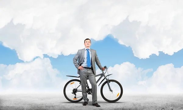 Confident and successful man in business suit standing with bike. Businessman with bicycle on background of blue sky. Male cyclist posing on camera with bicycle. Man relaxing outdoors in sunny day.