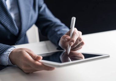 İş elbisesi giyen adam tabletle masada oturuyor