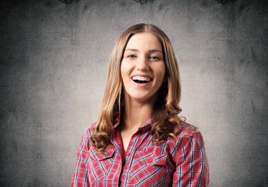 Mutlu sevimli kız geniş gülümseyen. Duygusal genç kadın yüz ifadesini şaşırttı. Güzel kız portresi gri arka plan üzerinde kırmızı damalı gömlek giyer. İnsanlar duygu ve ifade.