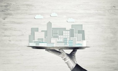 Elle tutulan metal tepsi ahşap arka planda modern şehir modeli.