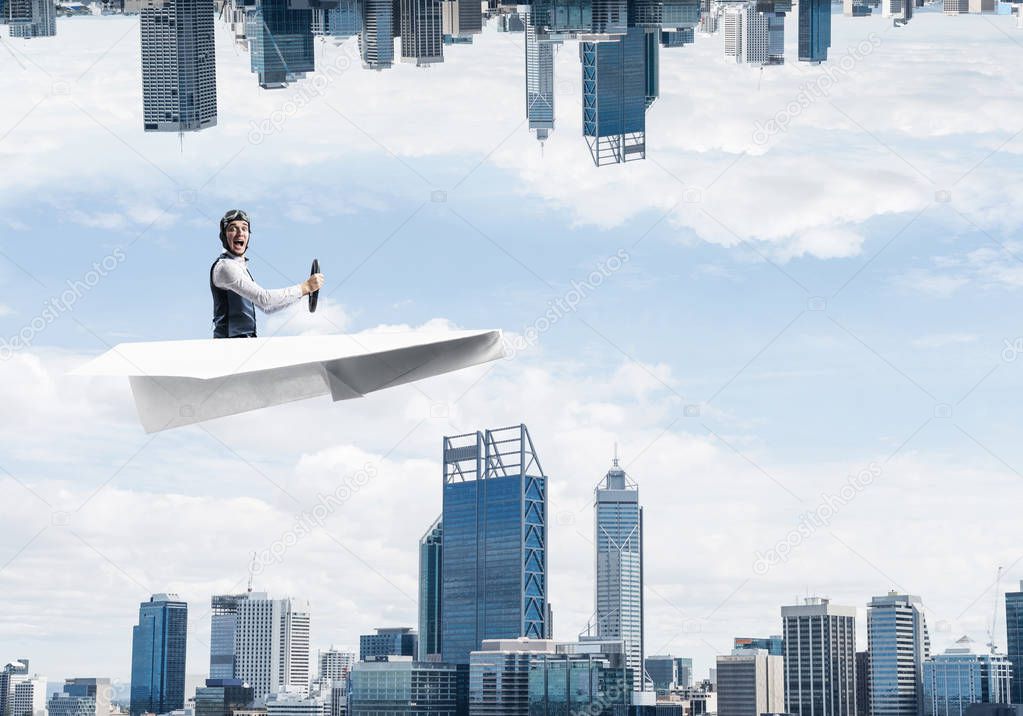 Businessman flying in paper plane. Two modern urban worlds located upside down to each other. Funny man in aviator hat and goggles driving paper airplane. Business center with skyscrapers