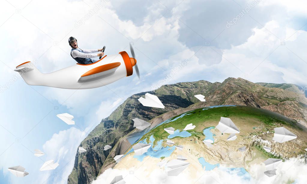 Happy pilot driving small propeller plane on background of blue sky with clouds. Traveling around the world by airplane. Funny man flying in small airplane. Round earth with mountain landscape.