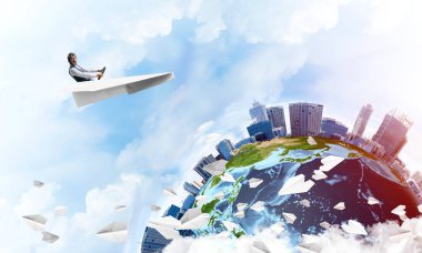 Havacı şapkalı işadamı kağıt düzlemde oturuyor ve direksiyonu tutuyor. Bulutlu mavi gökyüzünde kağıt uçak kullanan pilot. Yüksek gökdelenler ve deniz hattı ile modern şehrin küresel görünümü.