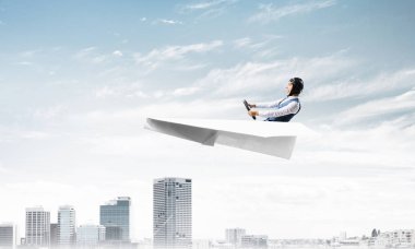 Havacı şapkalı işadamı ve gözlüklü, şehir merkezinin üzerinde yüksek binalarla kağıt uçak sürüyor. Mavi gökyüzü ile modern megalopolis panorama. Karışık medya iş kavramı. Hayal ve hayal gücü.