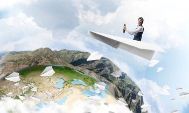 Pilot deri kask ve gözlük mavi bulutlu gökyüzünün arka planda kağıt uçak sürüş. Dünyayı dolaşıyor. Küçük kağıttan uçakta uçan komik adam. Yüksek dağ sırası ile Dünya ufku