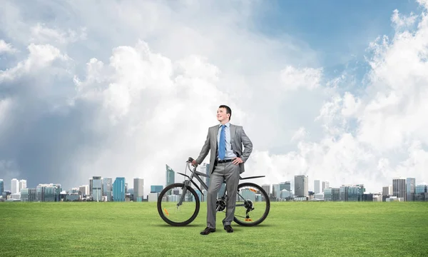 Good looking caucasian man in business suit posing on green meadow with bike. Happy businessman with bicycle relax on green grass at sunny day. Ecology transportation and environmental protection