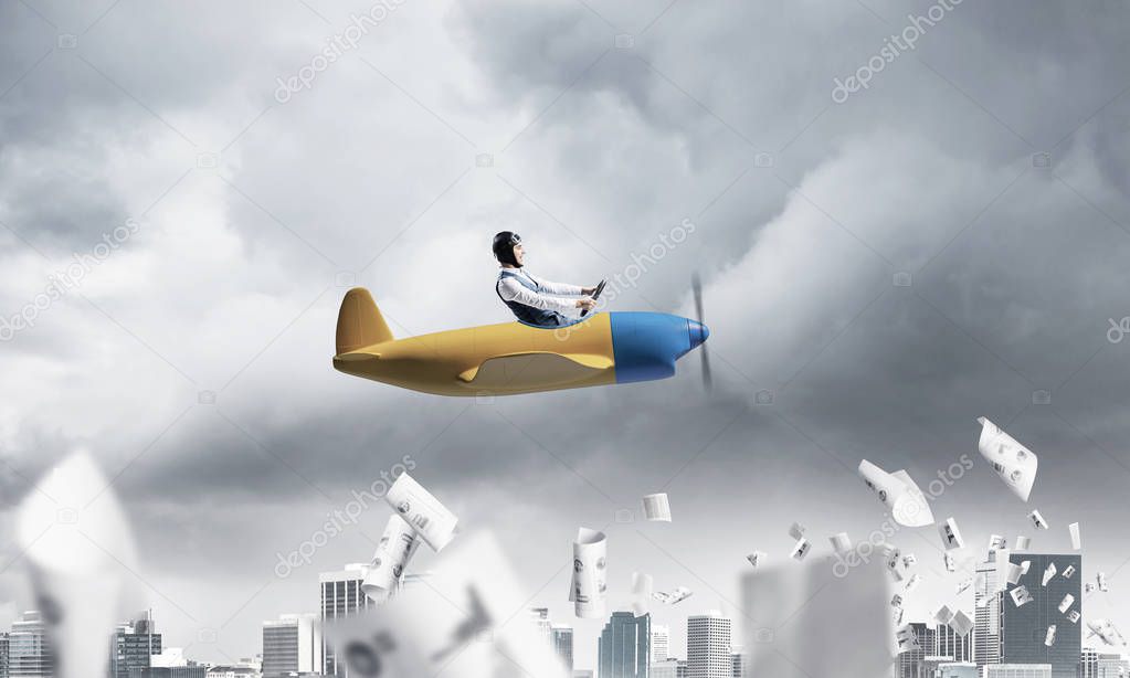 Crisis management and control in difficult situation concept. Businessman in aviator hat driving propeller plane in storm. Pilot flying in small airplane. Megalopolis panorama with dramatic sky.