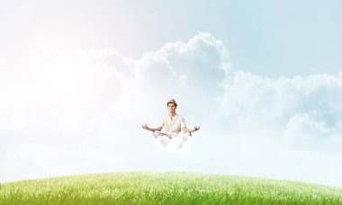 Genç adam gözleri koruma kapalı ve seyir arka plan üzerinde parlak ve güzel manzara ile havada bulut üzerinde meditasyon sırasında konsantre.