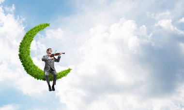 Genç adam takım elbise ve yeşil ay üzerinde oturan ve Keman çalmaya gözlük