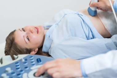 Ultrason muayenesinde mutlu bir kadın. Ultrason makinesiyle doğum öncesi teşhisi. Düzenli muayene ve hastalık önleme. Gülümseyen hamile kadın hastaneye gidip karın sonografisi yapıyor..