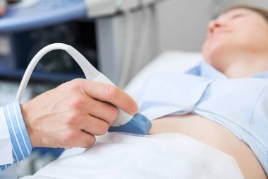 Sonograf iş yerinde ultrason makinesi kullanıyor. Modern klinik tanı ve tedavi. Doktorun elinde ultrason tarayıcısı var. Doktor ultrason hastanede kadın hasta karnını muayene ediyor..