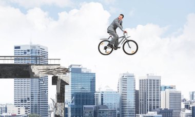 İşadamı işe bisikletle gidiyor. Havada bisiklete binen iş elbisesi giyen mutlu adam. Yakışıklı bisikletçi arka plan modern şehir panorama ve mavi bulutlu gökyüzüne bakıyor.