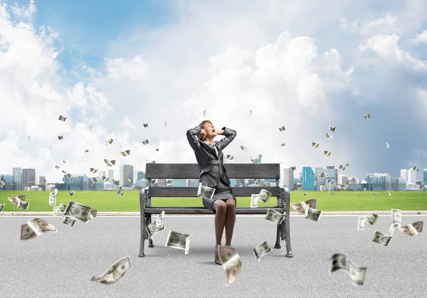 Stressful woman sitting on wooden bench. Emotional screaming girl keeps hands on head. Businesswoman in despair on background cityline panorama with falling money banknotes. Woman call for help.