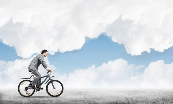 Businessman commuting to work by bike. Man in business suit riding bicycle on road. Handsome cyclist on background of blue sky. Nature landscape with copy space. Eco-friendly transport and active life