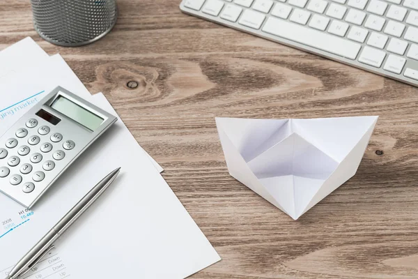 Wooden office desk with white origami boat.