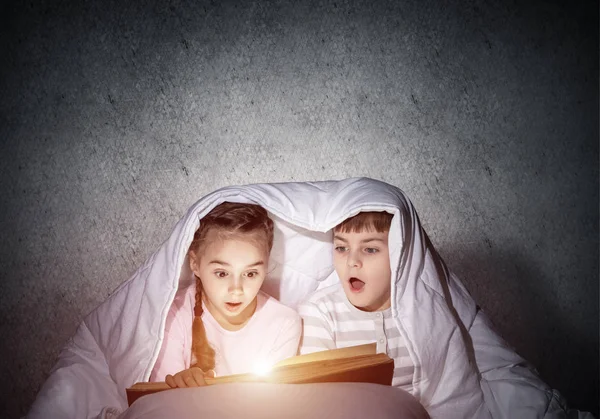 Des enfants surpris lisant des histoires effrayantes au lit — Photo
