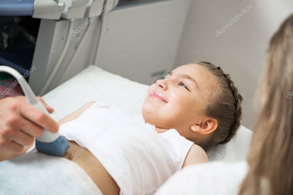 Doctor ultrasound examines little patient belly at hospital. Abdominal cavity diagnosis in clinic with modern equipment. Close-up happy little girl lying on bed. Highest quality children healthcare.