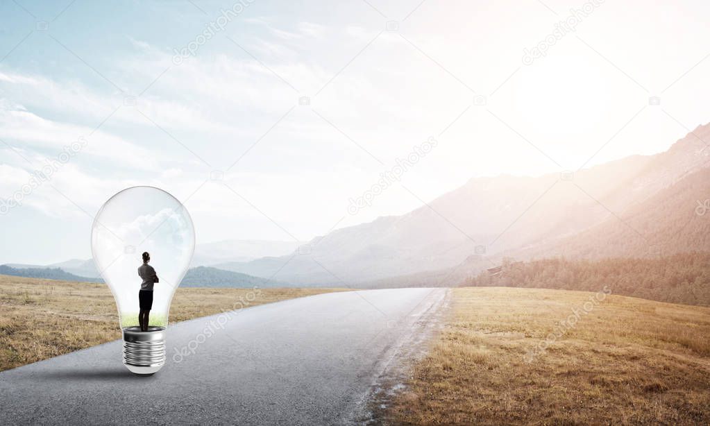 Young businesswoman trapped inside of light bulb on countryside road