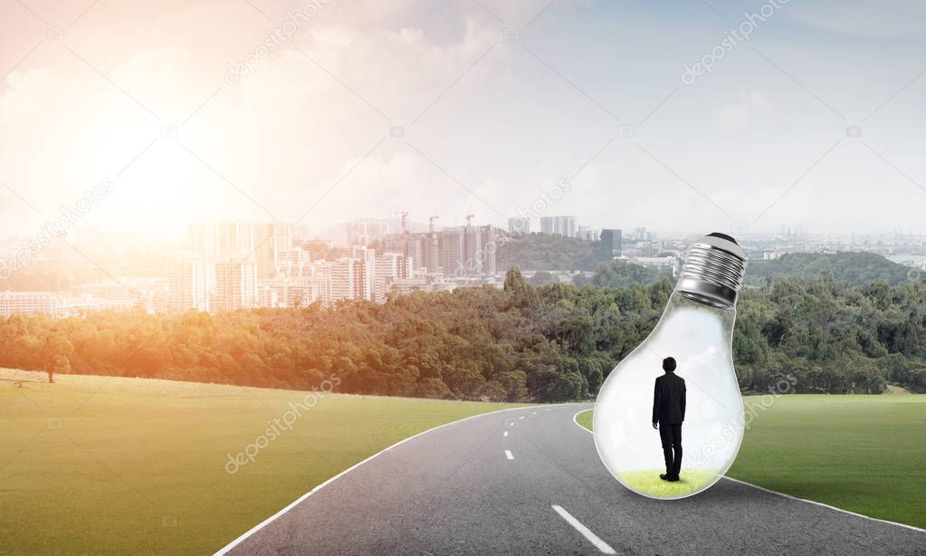Young businessman trapped inside of light bulb on asphalt road