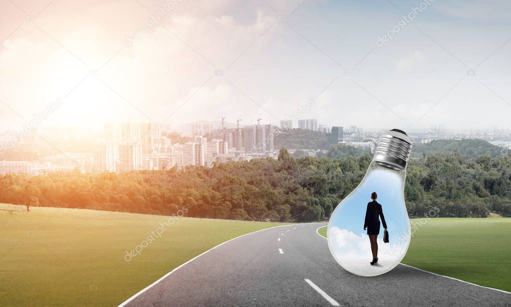 Young businesswoman trapped inside of light bulb on asphalt road