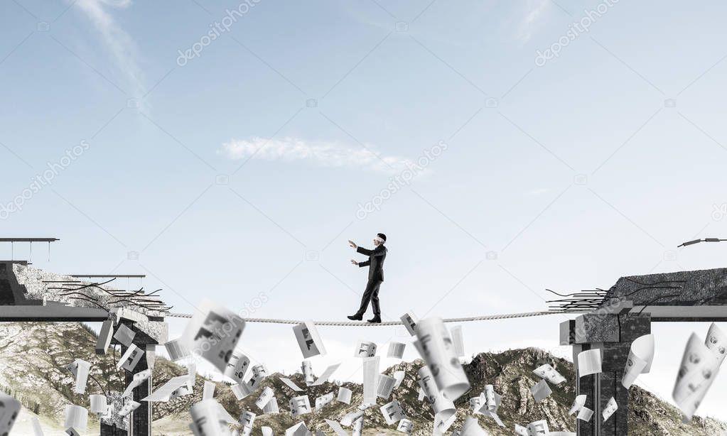 Businessman walking blindfolded on rope among flying papers and above huge gap in bridge as symbol of hidden threats and risks. Nature view on background. 3D rendering.