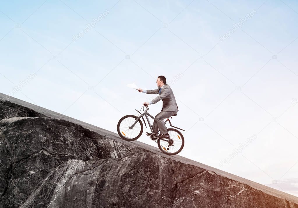Businessman with paper documents in hand going uphill on bike. Paperwork express service. Corporate employee in grey business suit on bicycle riding up on mountain road. Accounting deadline concept.