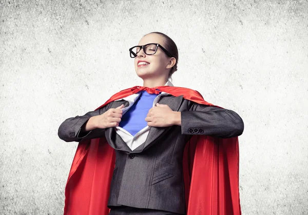 Portrait of business woman super heroine tearing off her shirt. Smiling business lady with closed eyes in red hero cape on grey wall background. Brave super woman dreaming about new wins