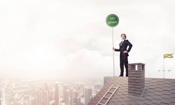 Επιχειρηματίας με κοστούμι στο σπίτι κορυφή με πινακίδα έννοια οικολογία. — Φωτογραφία Αρχείου