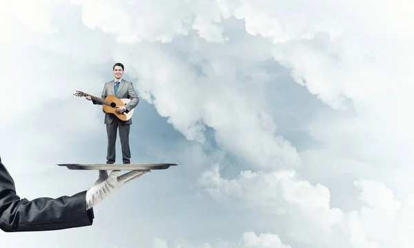 Uomo d'affari su vassoio di metallo suonare la chitarra acustica contro sfondo cielo blu — Foto Stock