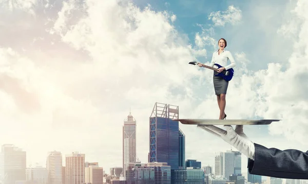 Attraktive Geschäftsfrau auf Metalltablett spielt E-Gitarre vor Stadtbild-Hintergrund — Stockfoto
