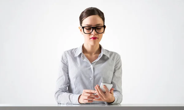 Jovem encantadora senta-se na mesa com smartphone — Fotografia de Stock